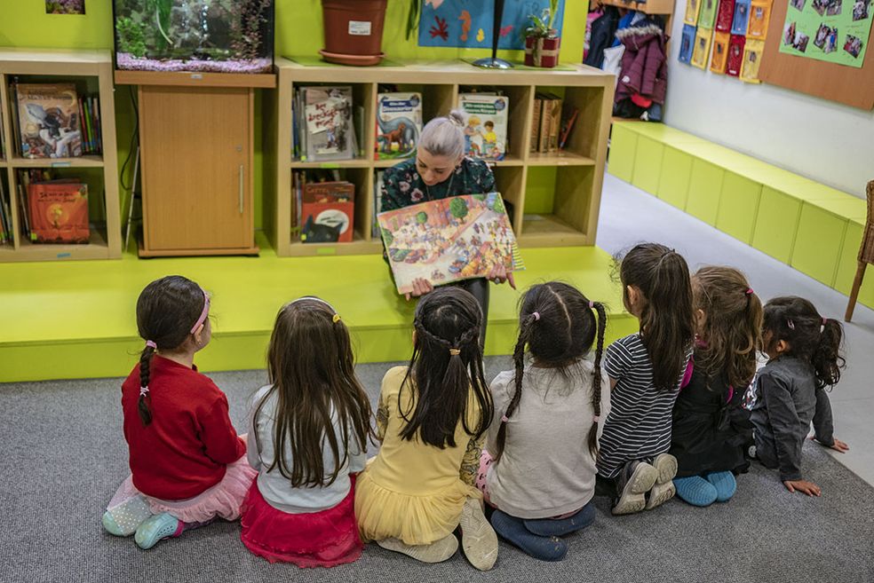 Bild: Eine Erzieherin erzählt eine Geschichte aus einem Buch an Kinder und zeigt dabei den Buchinhalt.